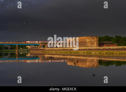 Virgin Trains Pendolino train Kreuze Carlisle Bridge, Lancaster, spiegelt sich in den Fluss mit einem stürmischen Himmel vorbei an den alten williamsons Gebäude Stockfoto