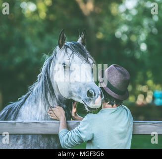 Junger Mann mit seiner arabischen Pferd im Sommer auf der Weide Stockfoto