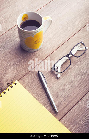 Business Desktop. Kaffeebecher, Brillen, Kugelschreiber und gelber Notizblock auf hölzernen Tisch. Von oben nach unten anzeigen. Stockfoto