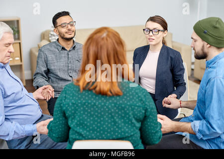 Gruppe von Patienten mit phobien im Kreis sitzen und halten sich an den Händen, während talentierte Psychologe Durchführung Sitzung, Interieur des gemütlichen Büro o Stockfoto