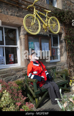 Alte Vogelscheuche auf Holz garten Sitz in Wray, Lancaster, Großbritannien sitzen. 28.04.2018. Wray Scarecrow Festival und Fair. Die Dorfbewohner von Wray sind wieder ein paar seltsame, verrückte und wunderbare Vogelscheuche Kreationen zu überraschen und zu erfreuen. Jedes Jahr Besucher wandern um Wray Dorf, die Entdeckung der Wirt der Vogelscheuchen, die in Gärten geknallt haben. Credit: MediaWorldImages/AlamyLiveNews Stockfoto