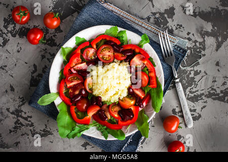 Couscous Salat mit Ruccola, Tomaten, Paprika und rote Bohnen in Weiß auf dunkelgrau konkreten Hintergrund Stockfoto