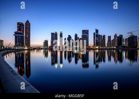 Die Lichter der Innenstadt von Dubai schimmern bei Sonnenuntergang auf der Kanaloberfläche und fangen die atemberaubende Skyline und die moderne Architektur der Stadt ein Stockfoto