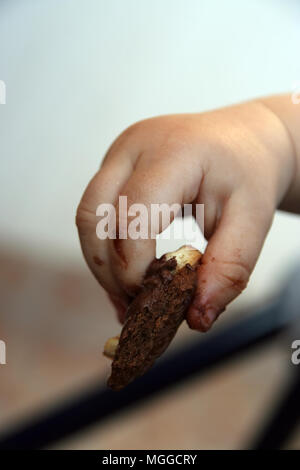 Kid chocolate Cookie in der Hand halten. Kinder Hand verschmiert mit Schokolade Cookie. Stockfoto