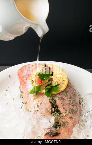 Ganze rohe organische fisch meer Zander auf Eis mit Zitrone, sy-Sauce, grünen, roten Pfeffer, in weiße Platte auf einem dunklen Hintergrund Tabelle. Ansicht von oben mit der Kopie Stockfoto