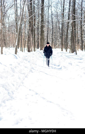 UFA, Russland, 29. MÄRZ 2018 - Ältere Menschen im Winter Kleidung geht mit Nordic Walking Stöcke durch einen Waldweg in schneefall Einsatz der Stöcke zu im Stockfoto