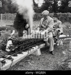 1950, historische, erwachsenen männlichen amteur rail Enthusiasten mit dem Dampfzug auf einer Miniatur-eisenbahn, England, UK. Stockfoto