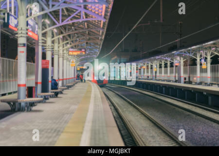 Bahnhof, Plattform in der Nacht, in der Dämmerung, Zug in der Ferne. Personenbeförderung, der Stil des Lebens. Unscharfe moderne Hintergrund Stockfoto