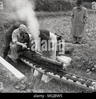 1950, historische, erwachsenen männlichen amteur rail Enthusiasten mit dem Dampfzug auf einer Miniatur-eisenbahn, England, UK. Stockfoto
