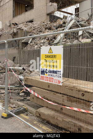 Sicherheitszaun mit Gefahr Abriss in Arbeit Zeichen vor Teilweise abgerissen mehrgeschossigen Stahlbetonbau und Beton Rubble uk Stockfoto