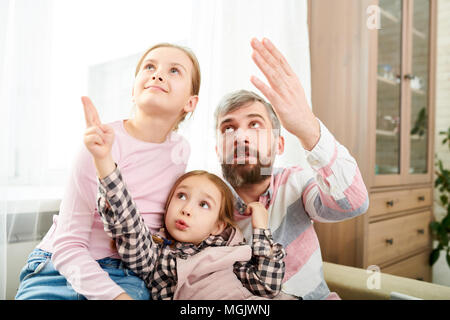 Sehr nette Familie von drei nach oben und zeigte auf etwas während versammelt im gemütlichen Wohnzimmer beleuchtet mit Sonnenstrahlen Stockfoto