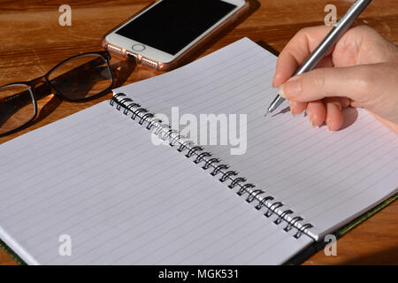 Frau mit Stift in der Hand, balanciert, in einer Spirale gebundenes Notizbuch zu schreiben Stockfoto