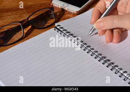 Frau mit Stift in der Hand, balanciert, in einer Spirale gebundenes Notizbuch zu schreiben Stockfoto