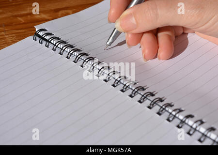 Frau mit Stift in der Hand, balanciert, in einer Spirale gebundenes Notizbuch zu schreiben Stockfoto