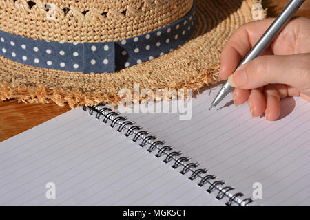 Frau mit Stift in der Hand, balanciert, in einer Spirale gebundenes Notizbuch zu schreiben Stockfoto