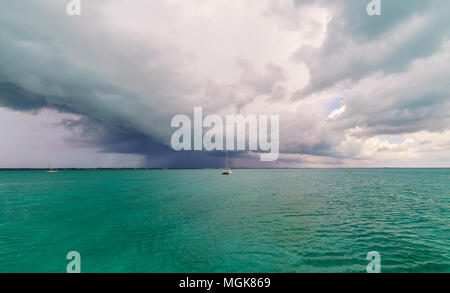 Eleuthera, Bahamas - Gewitterwolken bewegen Sie die Maus über einen verankerten Segelboot. Regen und texturierte Wolken im Hintergrund Stockfoto