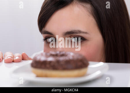 Nahaufnahme einer jungen Frau, die an Krapfen auf Platte Stockfoto