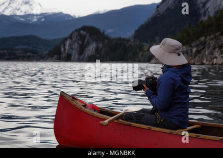 Männliche Fotografen auf ein hölzernes Kanu ist, die Bilder von der schönen kanadischen Bergwelt. In Squamish, nördlich von Vancouver, BC, Kanada Stockfoto