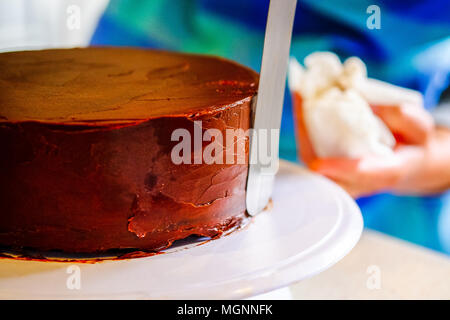 Eine Frau, die Ganache Vereisung oder Zuckerguss um einen Kuchen, mit einem Spatel Stockfoto