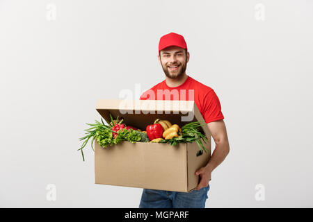 Lieferung Konzept: Stattlichen kaukasischen Lebensmittel-lieferservice Kurier Mann in der roten Uniform mit Lebensmittelgeschäft, mit frischem Obst und Gemüse Stockfoto