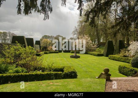 Formeller englischer Garten mit topiarem, gepflegtem Rasen und Frühlingsblüte unter dramatischem Himmel in einem historischen Anwesen. Stockfoto