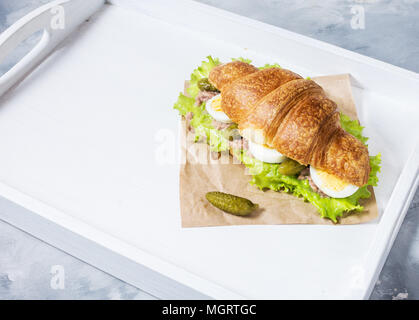 Croissant Sandwich mit Thunfisch, hart gekochte Eier, Salat und Gurke auf weißen Fach Frühstück Konzept. Platz kopieren Stockfoto