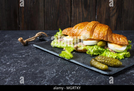 Croissant Sandwich mit Thunfisch, hart gekochte Eier, Salat und Gurke auf Tisch aus Stein. Platz kopieren Stockfoto