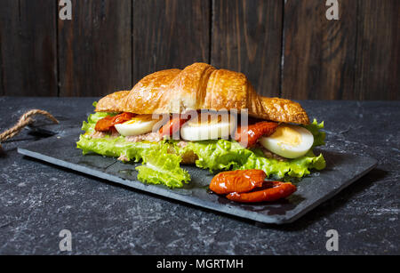 Croissant Sandwich mit Thunfisch, hart gekochte Eier, Salat und getrocknete Tomaten auf Tisch aus Stein. Stockfoto