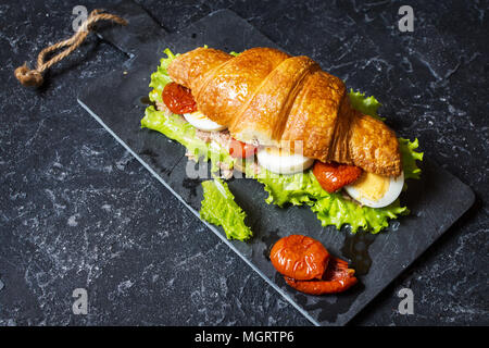 Croissant Sandwich mit Thunfisch, hart gekochte Eier, Salat und getrocknete Tomaten auf Tisch aus Stein. Stockfoto
