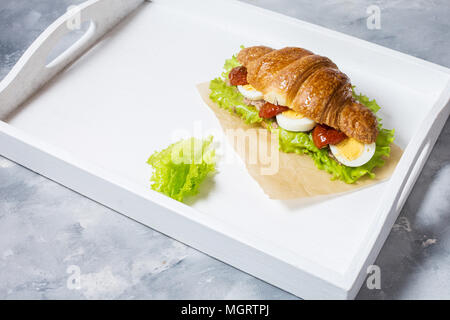 Croissant Sandwich mit Thunfisch, hart gekochte Eier, Salat und getrocknete Tomaten auf weißem Tray Frühstück Konzept. Platz kopieren Stockfoto
