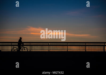 Alte Männer ist mit dem Fahrrad auf einer Brücke, mit wunderschönen blauen Himmel und Wolken im Hintergrund bei Sonnenuntergang, Silhouette Stockfoto