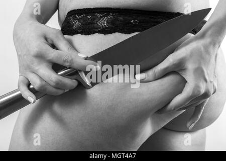 Schneiden mit dem Messer überdimensionale weibliche Gesäß mit Cellulite auf weißem Hintergrund, Monochrom Stockfoto