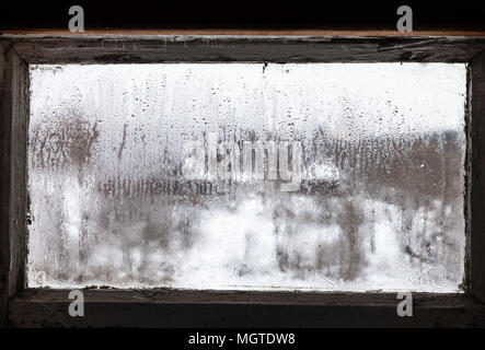 Verschwommene Sicht der russischen Dorf durch Wassertropfen auf Beschlagenen gefrorenen Fenster der ländlichen Haus in kalten Wintertag (Fokus auf Eis auf dem Glas) Stockfoto
