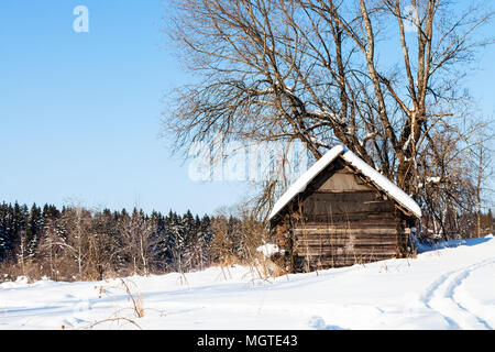 Alten, verlassenen Holzhütte in der Nähe von Forest im sonnigen Wintertag im kleinen Dorf in Smolensk Region Russlands Stockfoto