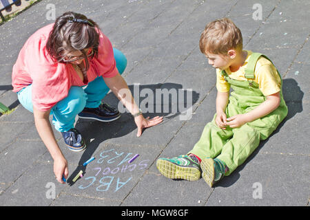 Mama und cute Boy zeichnen Alphabet mit bunter Kreide auf Asphalt. Sommer Aktivität und kreative Spiele für kleine Kinder. Zeit mit der Familie. Happy Mother's Day. Stockfoto