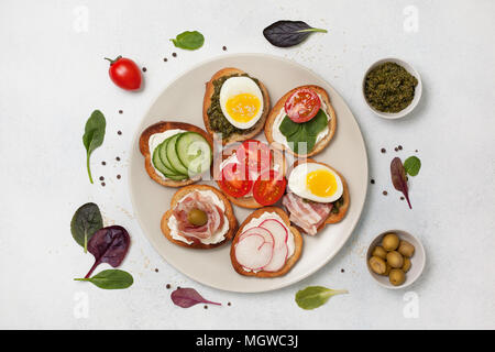 Varianten von Sandwiches mit Frischkäse, Pesto, Tomaten, Gurken, Ei, Speck, Rettiche auf einem hellen Hintergrund. Ansicht von oben Stockfoto