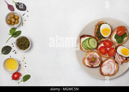 Varianten von Sandwiches mit Frischkäse, Pesto, Tomaten, Gurken, Ei, Speck, Rettiche auf einem hellen Hintergrund. Ansicht von oben Stockfoto