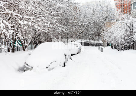 Schneebedeckte Autos am Parkplatz entlang der Straße im Wohnviertel der Stadt Moskau bei bedecktem Winter Tag Stockfoto