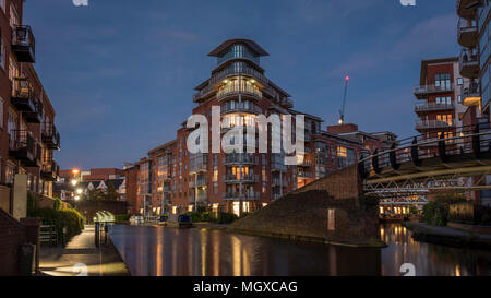 Modernes Apartment Gebäude, leuchtet in der Dämmerung, mit Blick auf eine städtische Wasserstraße, Kanal, in Birmingham, England, Großbritannien Stockfoto