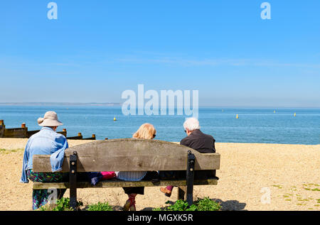 Gruppe von Menschen sitzen auf einer Bank am Meer, Whitstable Kent Stockfoto