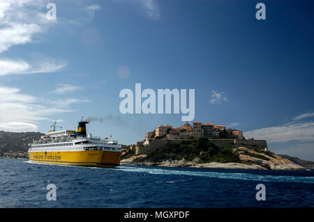 Ein Passagier- und Autofähre, Corsica Ferries und Sardinia Ferries nähert sich der Hafen von Calvi auf Korsika, wie es Segel an der Zitadelle von Calvi entfernt auf einem Hügel. Th Stockfoto