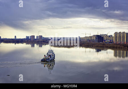 Ein mächtiger Fluss tugboat auf der sibirischen Fluss während der hohen Wasser. Im Hintergrund, moderne Stadt Gebäude Stockfoto