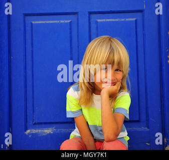 Süße Junge sitzt auf dem Boden mit dem tiefen Blau Holztür auf Hintergrund Stockfoto