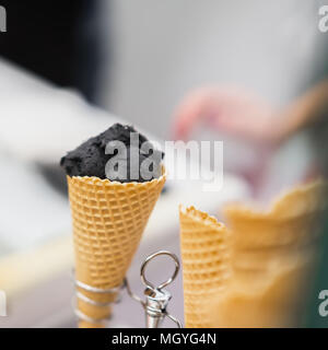 Close-up von Waffeln Kegel mit Ball von trendiges schwarzes Eis. Köstliche Kühlung teil an einem heißen Tag und nur zum Spaß. Selektive konzentrieren. Reale Szene in s Stockfoto