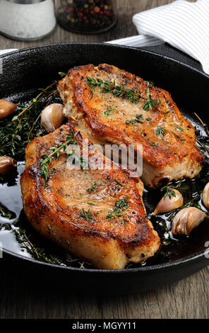 Saftig, brüniert Schweinesteak auf einen Knochen in Öl mit Knoblauch und Kräutern, die in der Pfanne. Stockfoto