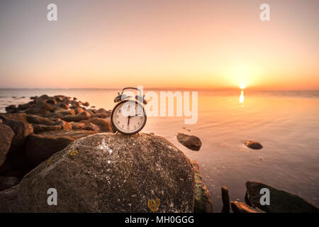 Wecker in den Sonnenaufgang am Meer auf einem großen Felsen am Ufer Stockfoto