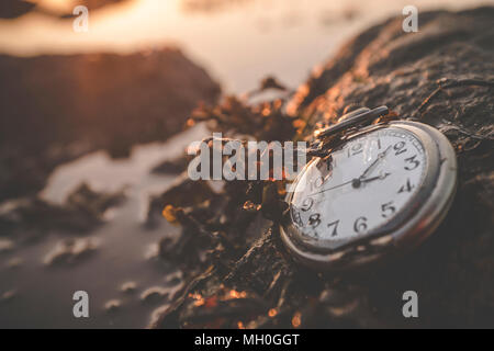 Alte Uhr auf einem Felsen am Meer im Sommer Sonnenaufgang mit Algen bedeckt Stockfoto