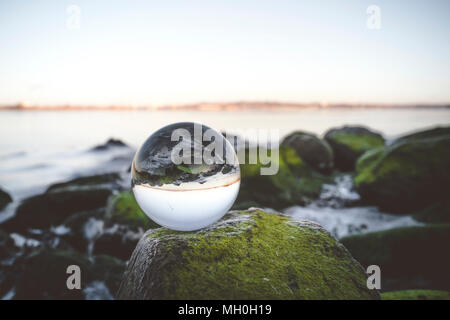 Crystal Ball auf Moos bedeckt Felsen am Meer am frühen Morgen Stockfoto