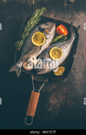 Blick von oben auf die Fisch mit Gemüse und Gewürze in Backform auf unebenem Untergrund. Stockfoto