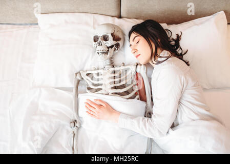 Frau schlafen in schlecht mit lustigen menschliches Skelett Stockfoto